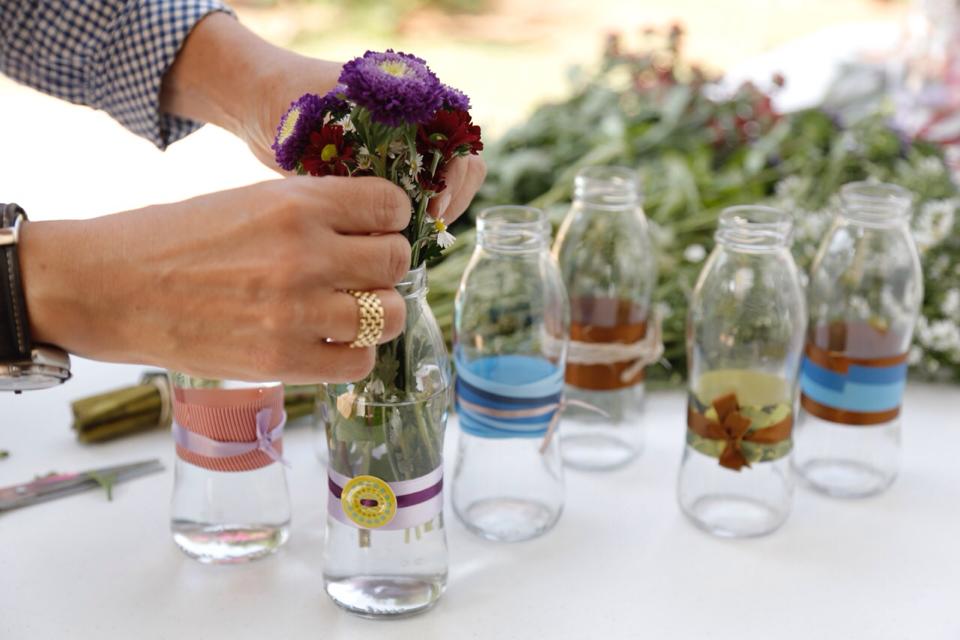 Com pequenas garrafas de vidro e flores, os arranjos do Flores para os Refugiados ganham forma. Crédito: Divulgação