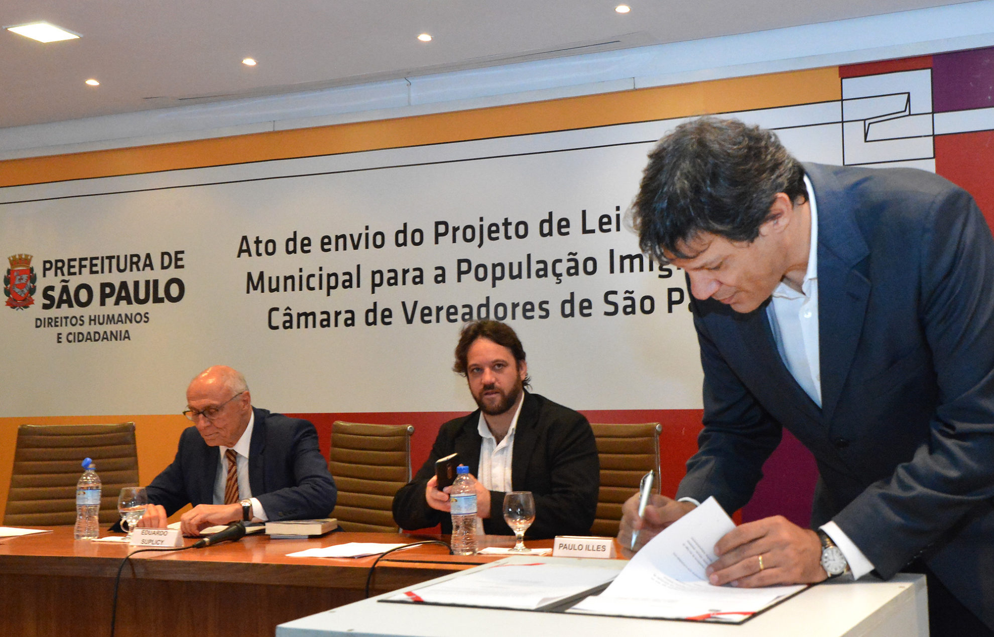 Haddad (d) assina projeto lei que cria política para imigrantes, acompanhado por Paulo Illes (c) e Suplicy (e). Crédito: Fernando Pereira/SECOM
