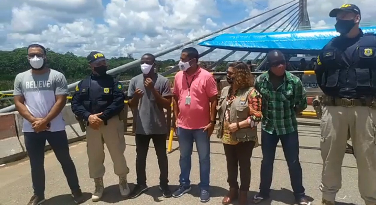 Imigrantes e autoridades brasileiras durante ato de desocupação da ponte que liga o Brasil ao Peru, no Acre